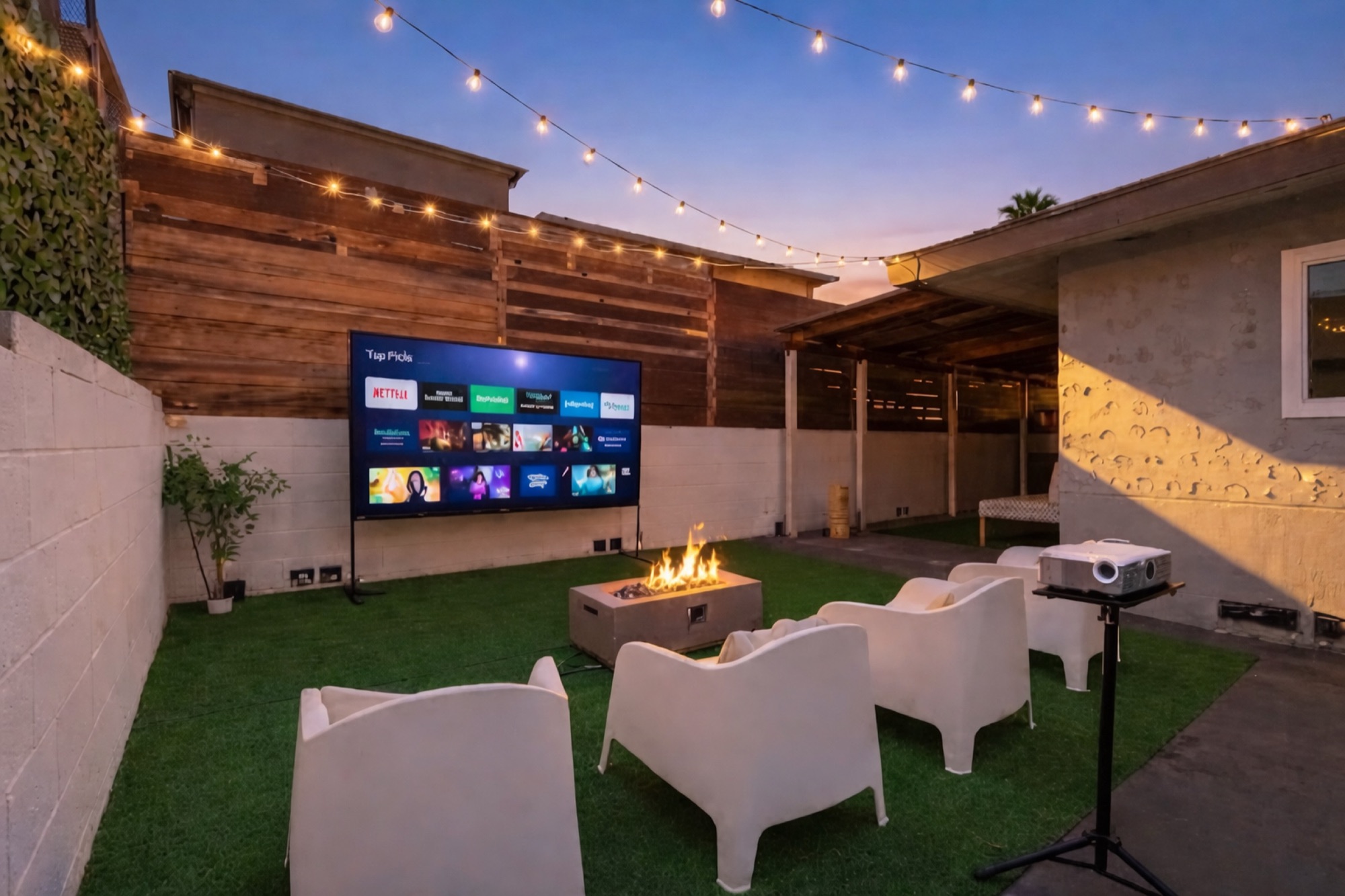 Our home's backyard at dusk: string lights, a fire pit, white lounge chairs and an outdoor movie screen.